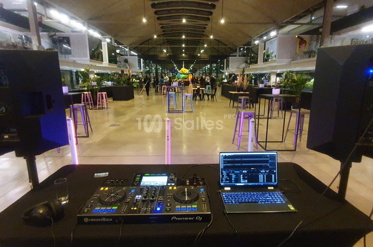 Table de mixage DJ avec ordinateur portable et haut-parleurs dans une salle moderne éclairée, prête pour un événement.
