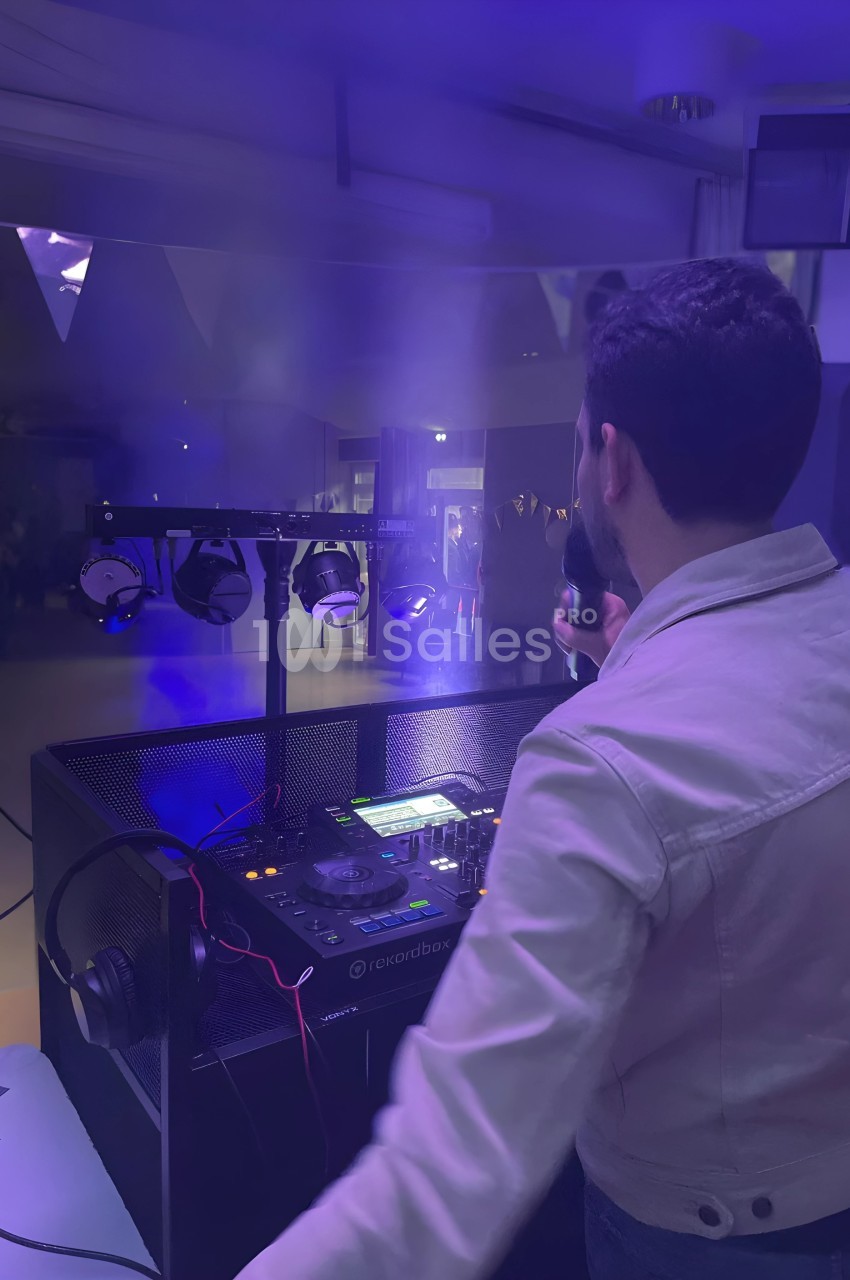 Un DJ de dos, tenant un micro, anime une soirée dans une ambiance lumineuse avec des projecteurs et de la fumée.