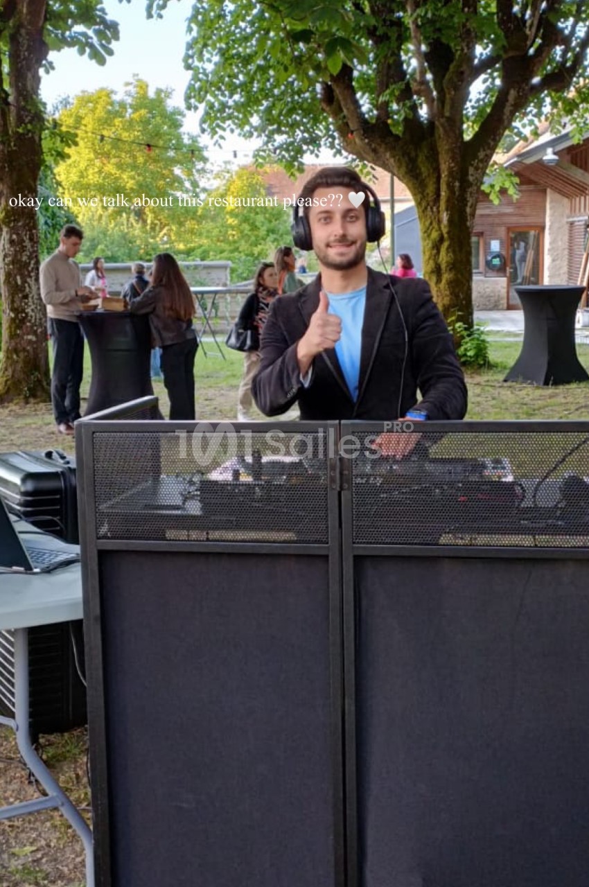 Un DJ souriant devant sa console dans un jardin, avec des invités discutant en arrière-plan.