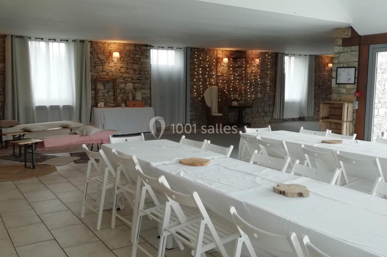 Salle de réception avec murs en pierre, tables blanches dressées et guirlandes lumineuses en arrière-plan.