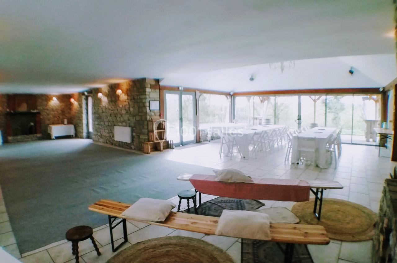 Salle spacieuse avec tables dressées, grandes baies vitrées, murs en pierre et espace aménagé avec bancs et coussins.