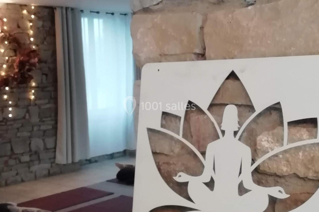 Salle de yoga avec tapis au sol, mur en pierre, lumière tamisée et panneau décoratif en forme de lotus.