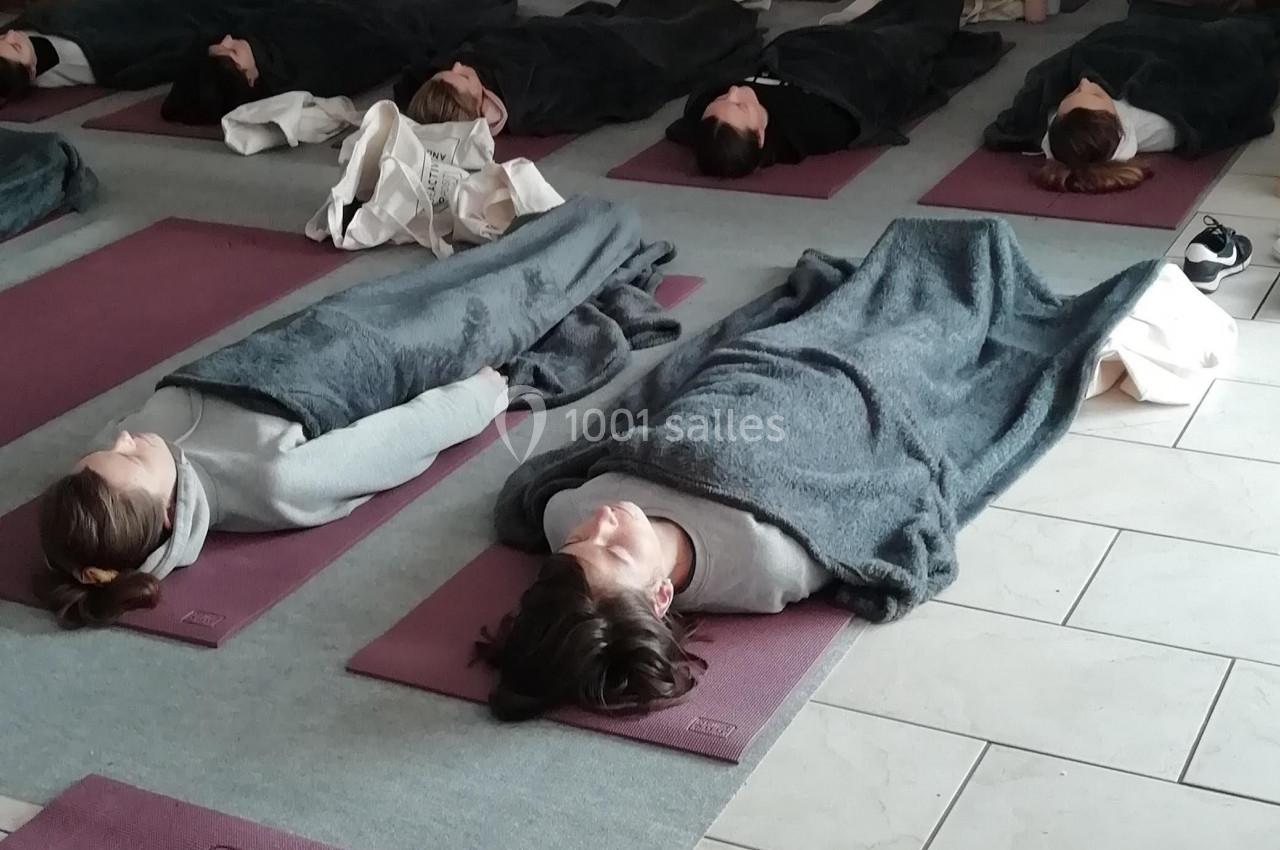 Personnes allongées sur des tapis de yoga, couvertes de couvertures, dans une salle éclairée de manière tamisée.