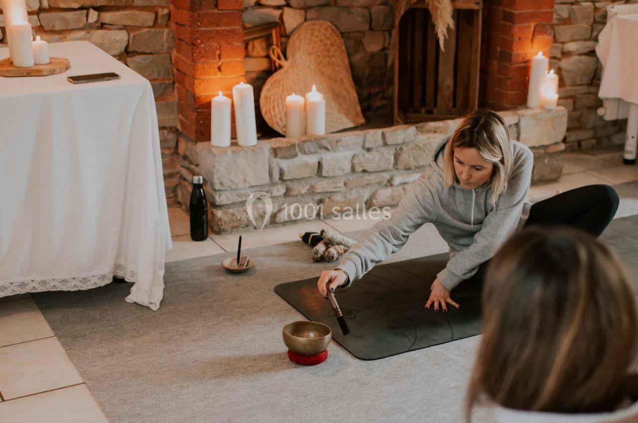 Une femme en tenue décontractée pratique une séance de méditation avec un bol tibétain dans une pièce chaleureuse.