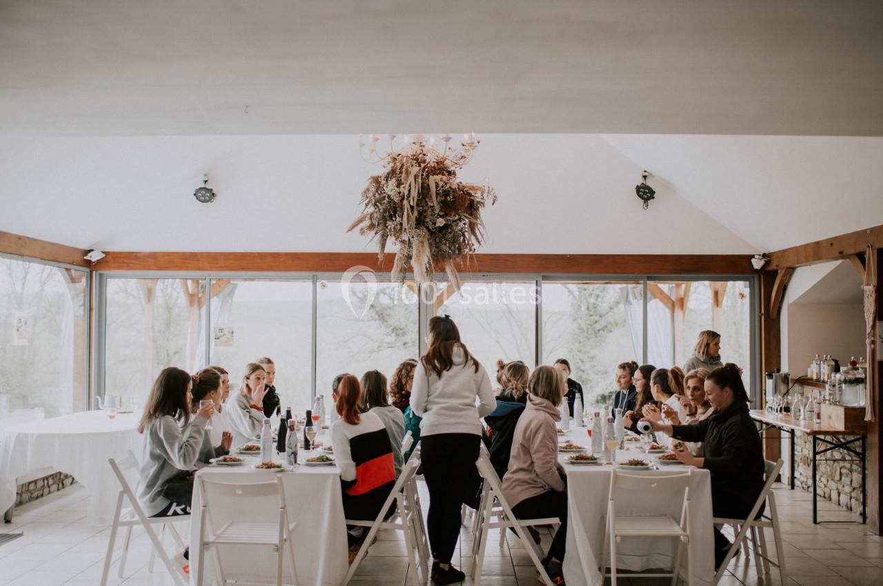 Un groupe de personnes partage un repas autour de tables dans une salle lumineuse avec de grandes baies vitrées.