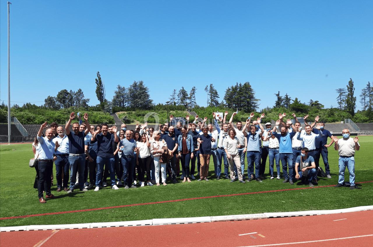 Un groupe de personnes souriantes lève les bras sur un terrain de sport par une journée ensoleillée.