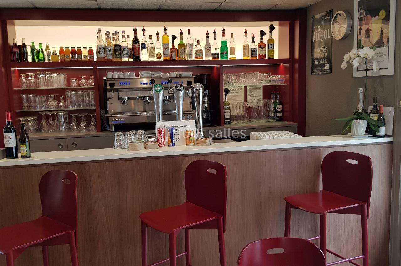 Comptoir de bar avec tabourets rouges, étagères garnies de bouteilles et verres, machine à café et tireuses à bière.