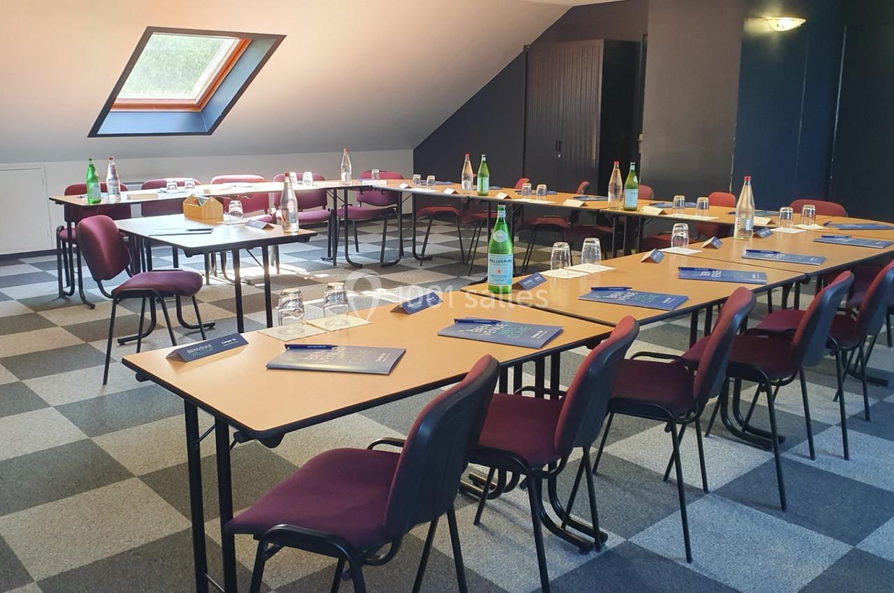 Salle de réunion avec tables disposées en U, chaises rouges, documents, bouteilles d'eau et lumière naturelle par une…