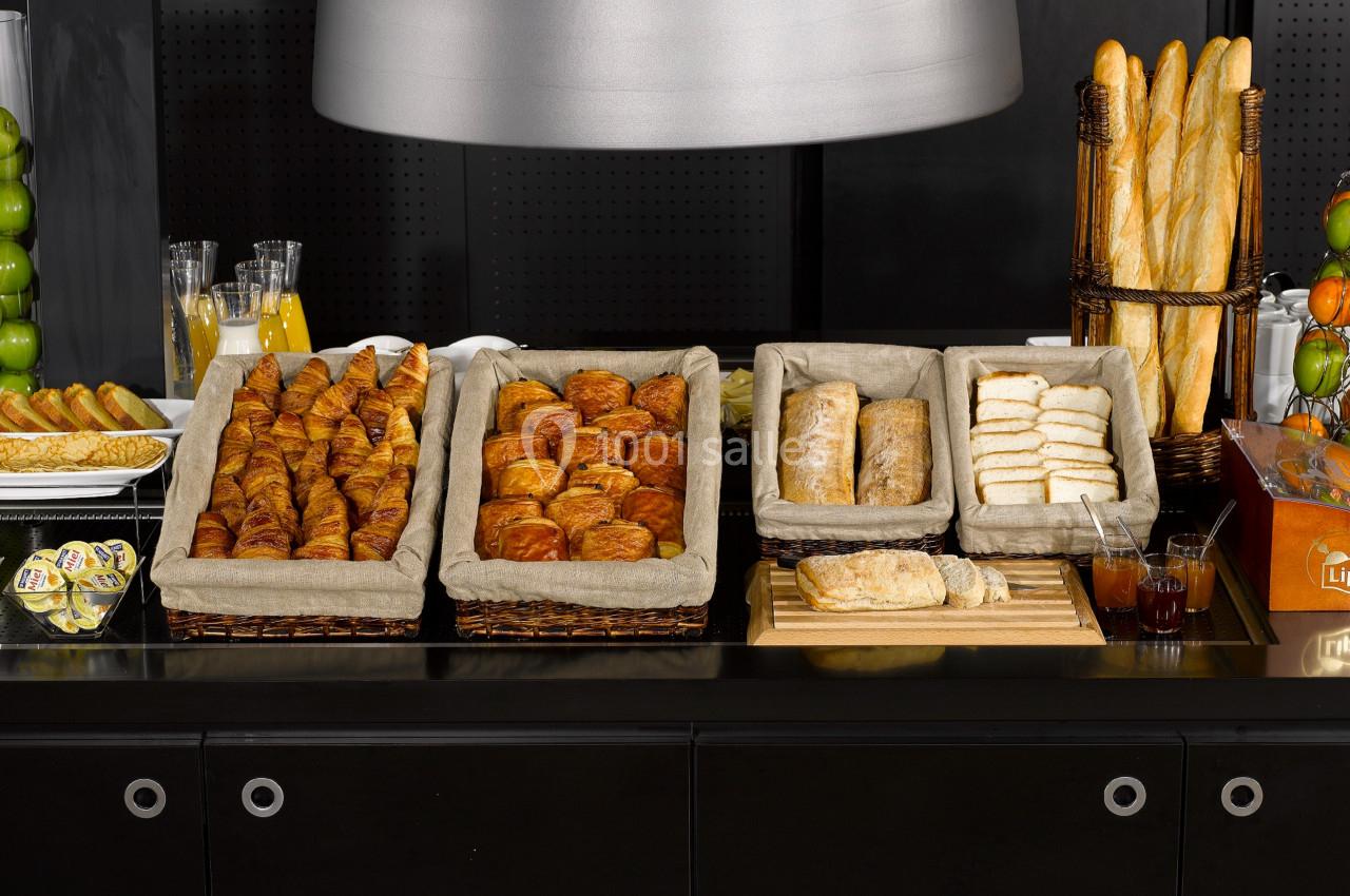 Buffet de viennoiseries et pains variés disposés sur un comptoir noir avec jus de fruits en arrière-plan.