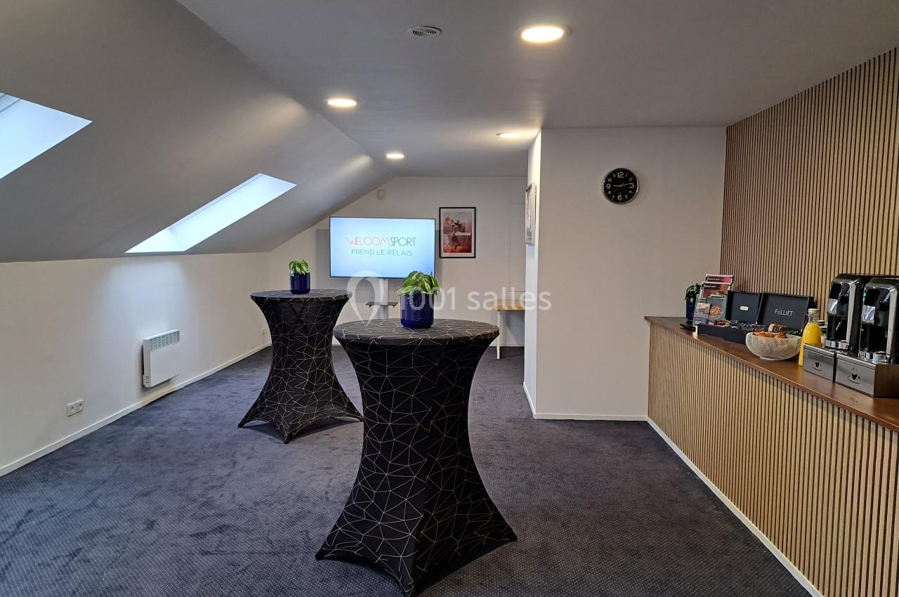 Salle de réunion lumineuse avec tables hautes, écran de présentation, coin café et décoration sobre.