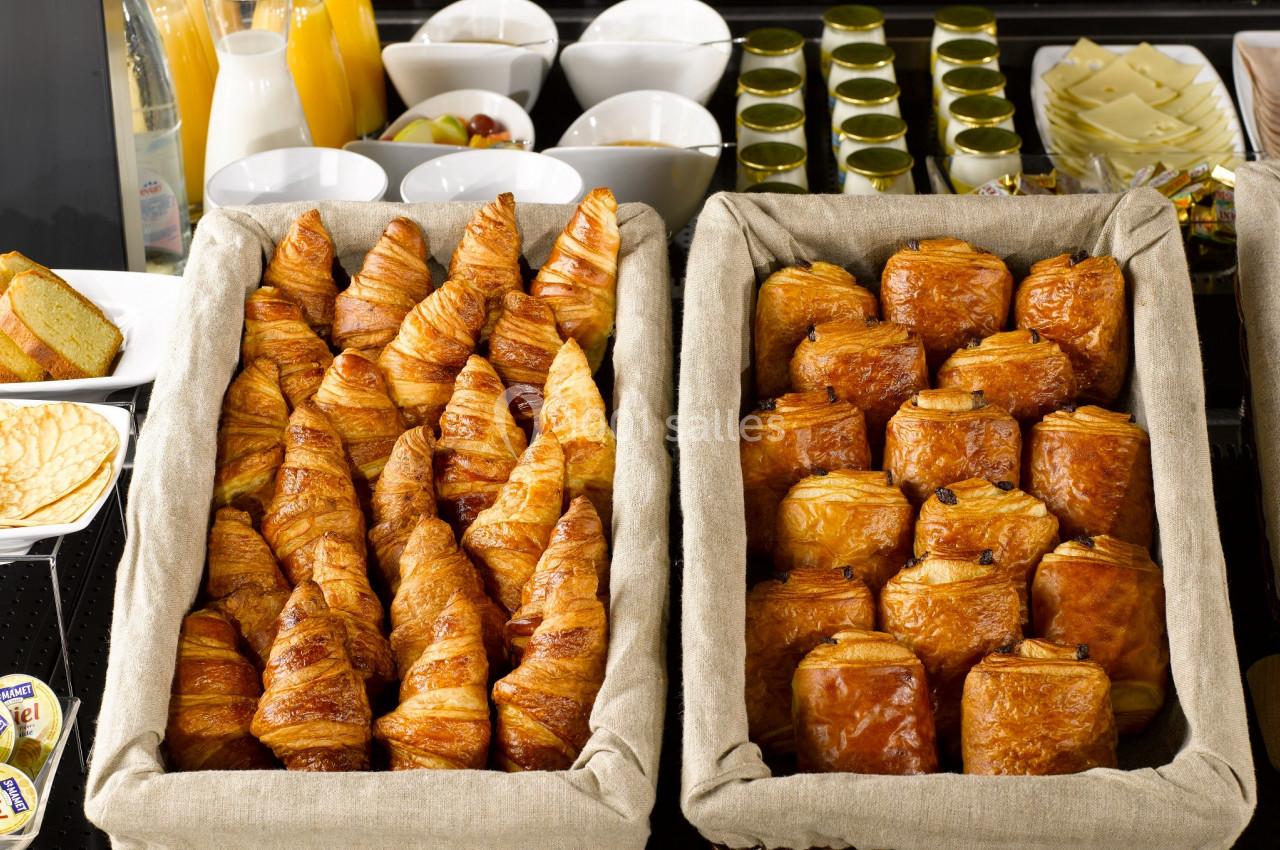 Corbeilles de croissants et pains au chocolat disposées sur un buffet avec boissons et condiments en arrière-plan.