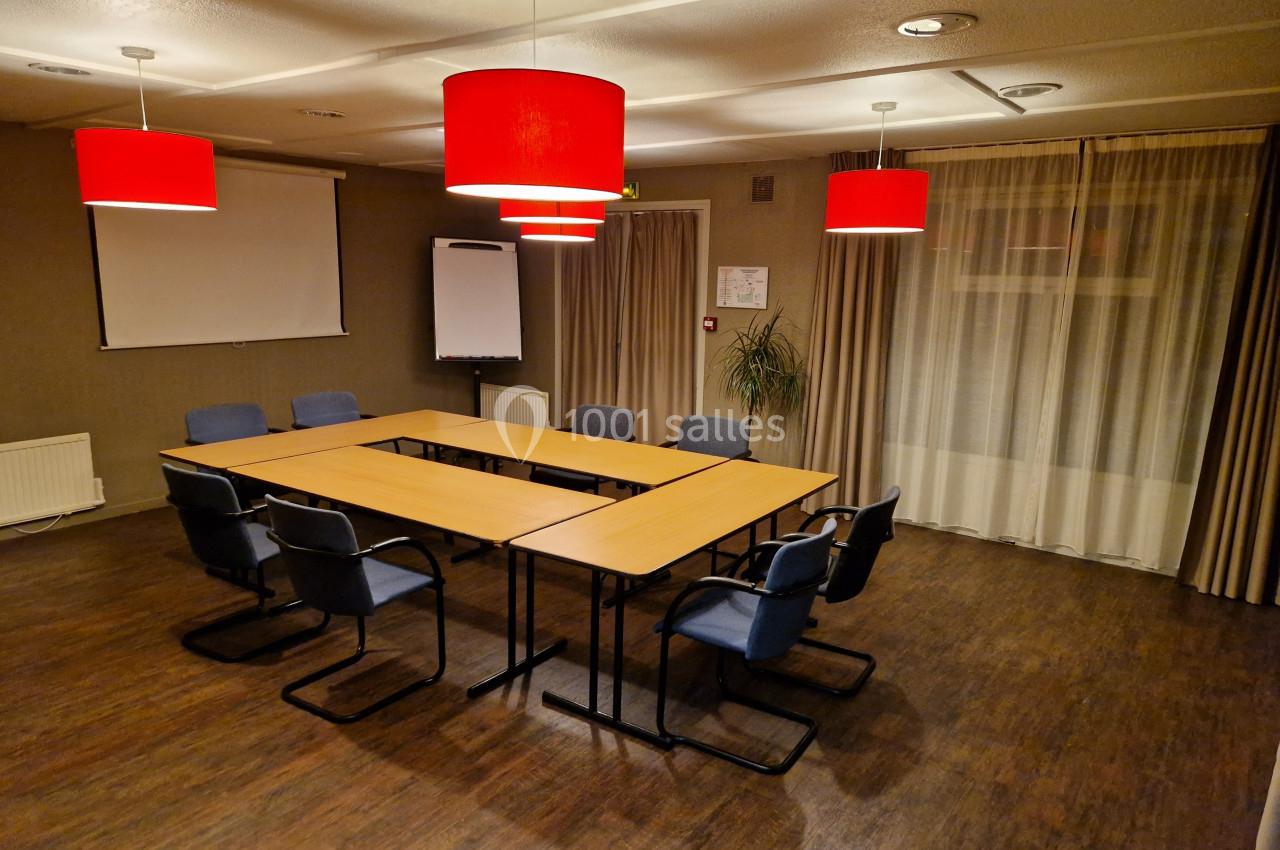 Salle de réunion avec tables en U, chaises bleues, éclairage par lampes rouges et tableau blanc en arrière-plan.