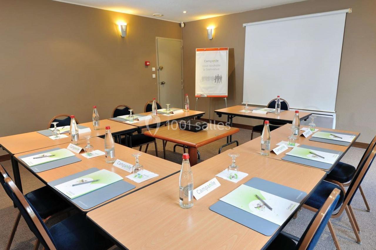 Salle de réunion équipée de tables disposées en U, avec documents, bouteilles d'eau et écran de projection.