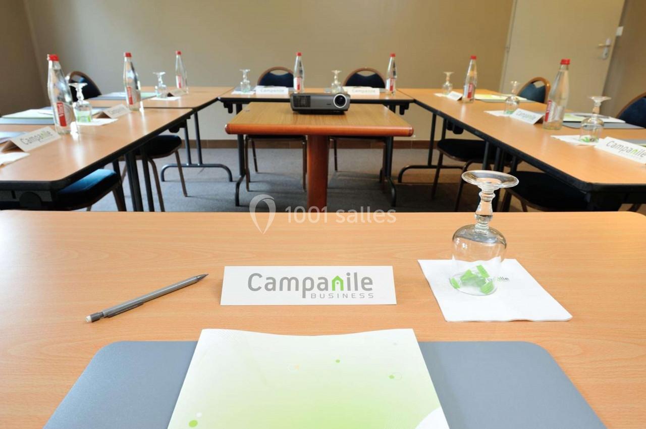 Salle de réunion avec tables disposées en U, équipée de bouteilles d'eau, verres, bloc-notes et un projecteur.