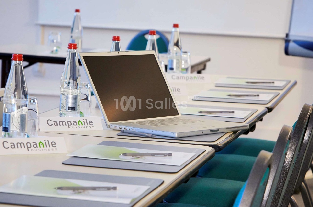 Salle de réunion avec un ordinateur portable ouvert sur une table, entouré de blocs-notes et de bouteilles d'eau.