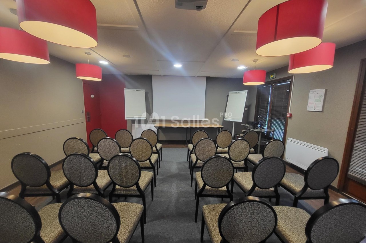 Salle de réunion avec des chaises disposées face à un écran de projection, entourée de lampes suspendues rouges.