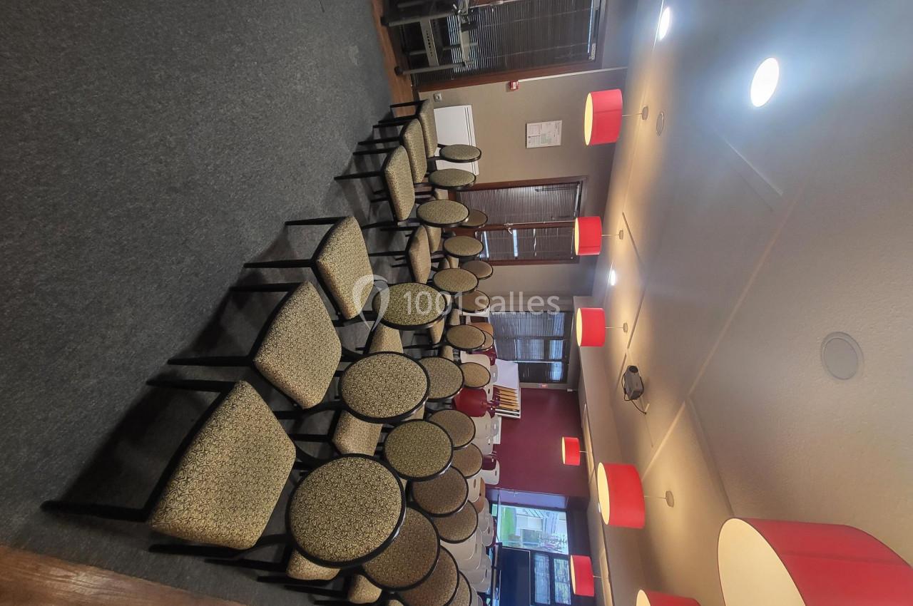 Salle de réunion avec des rangées de chaises rembourrées alignées, éclairée par des suspensions rouges.