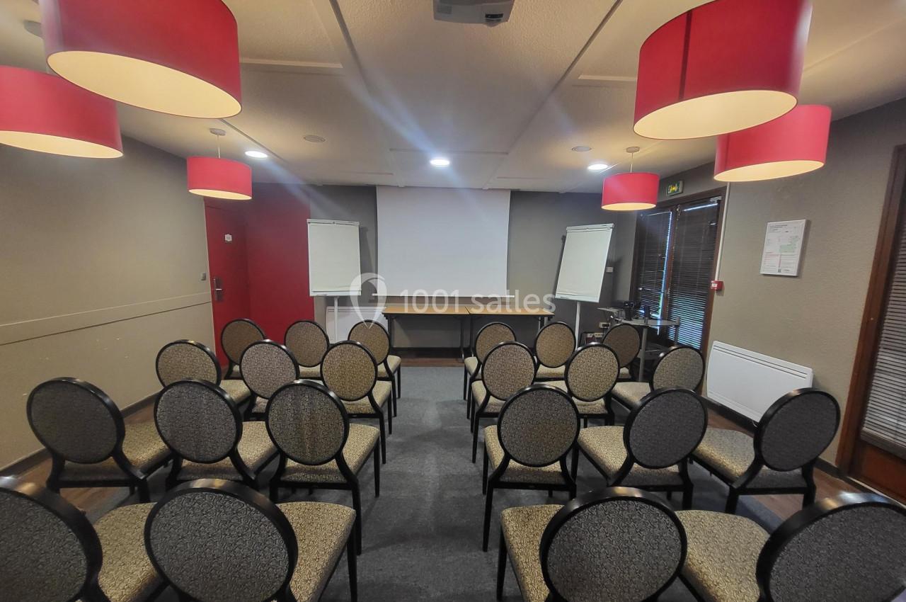 Salle de réunion avec des chaises disposées face à un écran de projection, entourée de lampes suspendues rouges.