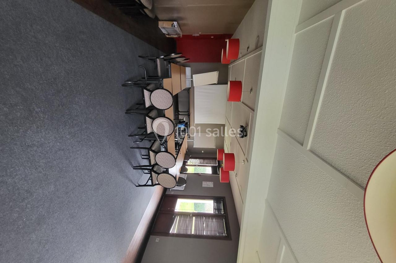 Salle de réunion avec chaises, tables, projecteur et fenêtres laissant entrer la lumière naturelle.