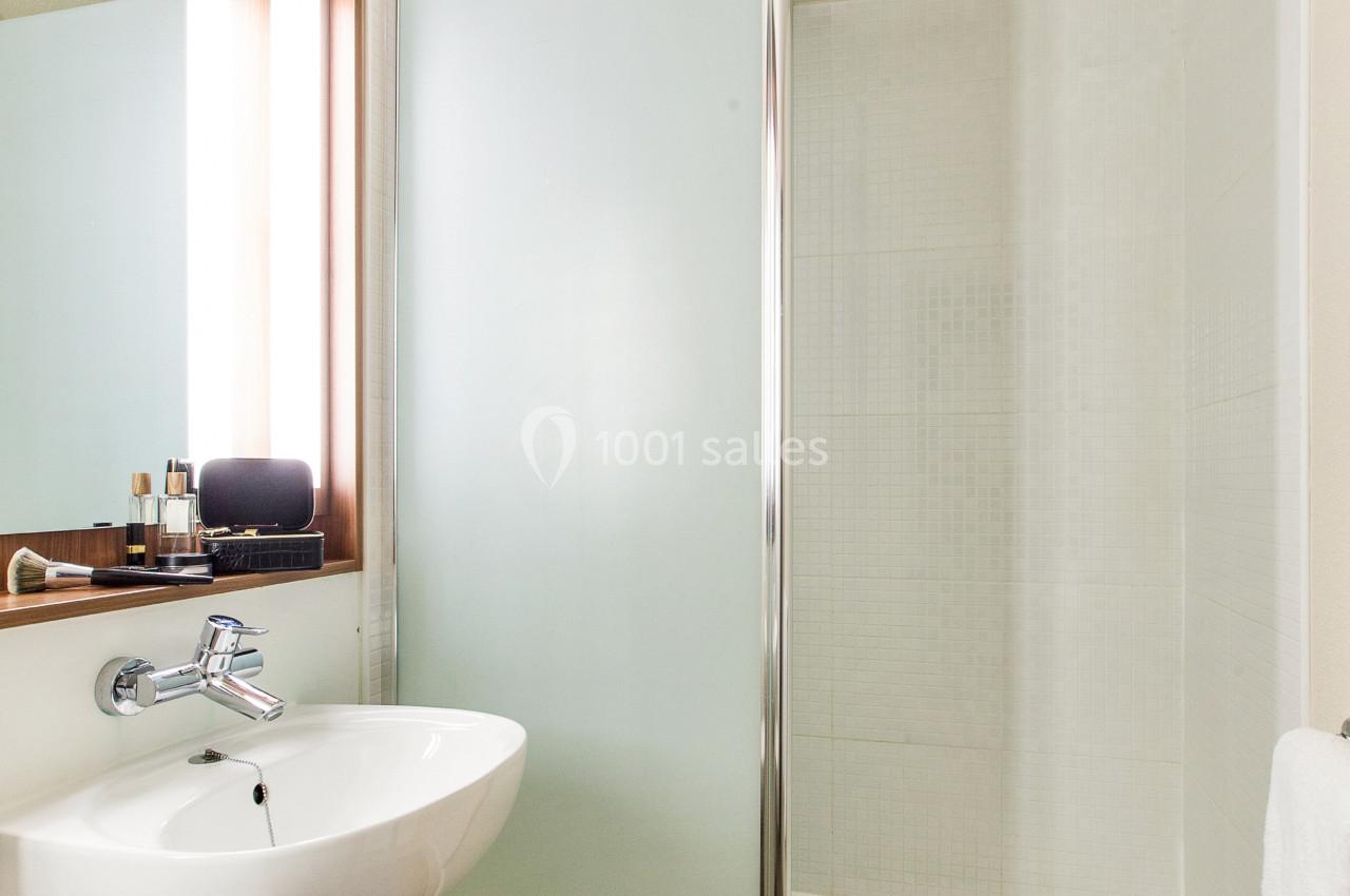 Salle de bain avec douche à paroi vitrée, lavabo suspendu, miroir éclairé et sol en carrelage foncé.