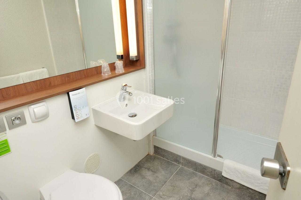 Salle de bain moderne avec lavabo, miroir, toilettes et douche vitrée sur un sol en carrelage gris.