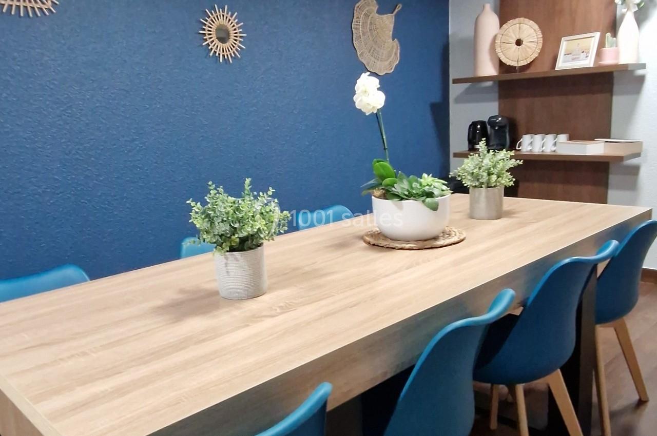 Salle à manger avec une grande table en bois, chaises bleues, mur bleu décoré et étagères en bois dans le fond.