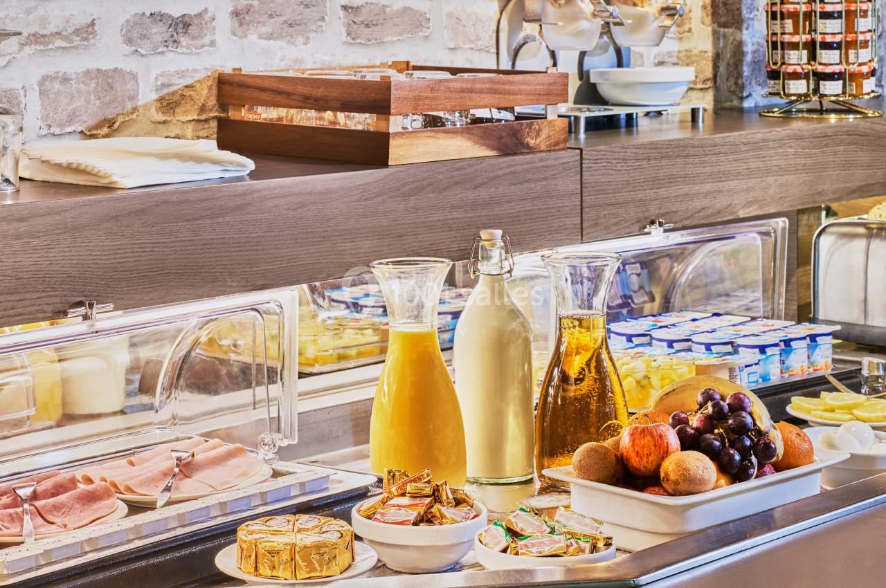 Buffet de petit-déjeuner avec jus, fruits, charcuterie, fromages et yaourts disposés sur un comptoir en bois.