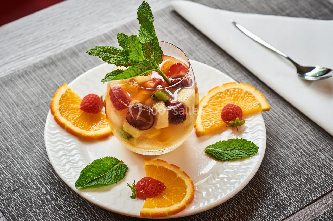 Verre de salade de fruits frais avec menthe, entouré de tranches d'orange, de framboises et de feuilles de menthe.