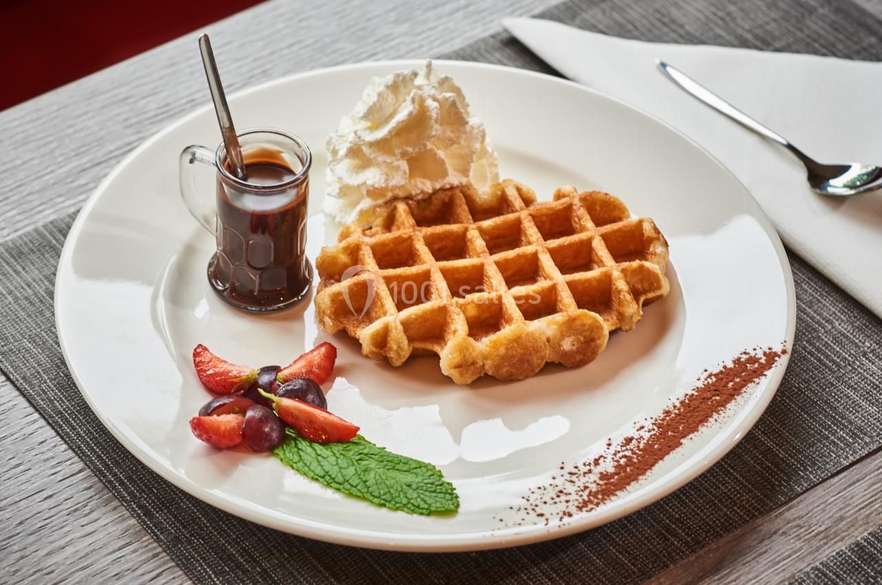 Assiette avec une gaufre, chantilly, sirop dans une cruche, fraises, raisins, feuille de menthe et poudre de cacao.
