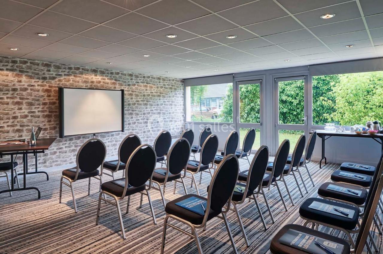 Salle de réunion lumineuse avec chaises disposées en rangées, écran de projection et table avec boissons.
