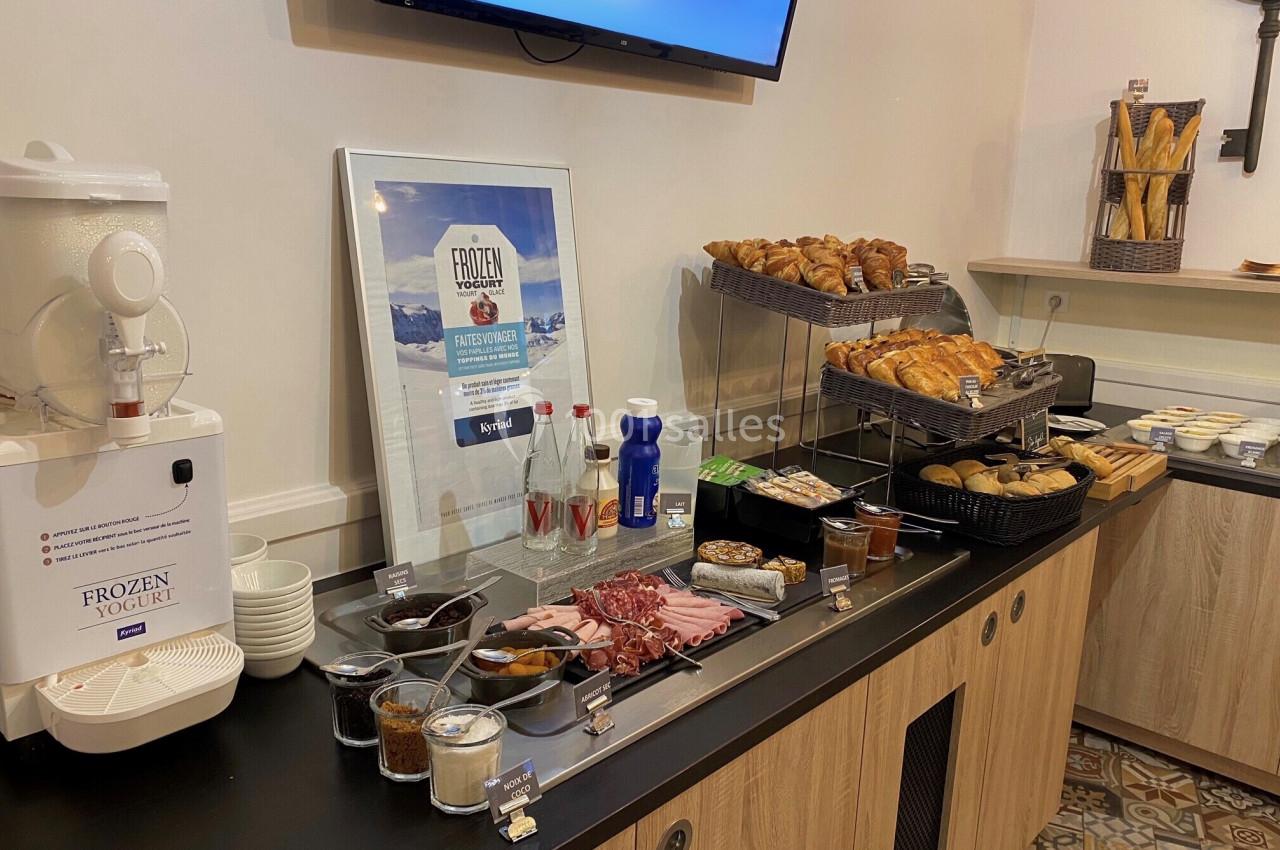 Buffet de petit-déjeuner avec viennoiseries, pains, charcuterie, yaourt glacé, boissons et condiments sur un comptoir.