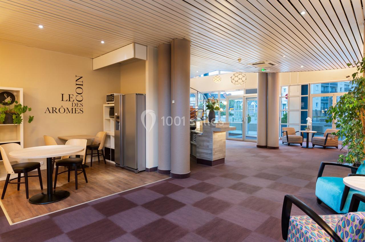 Espace intérieur lumineux avec tables, chaises, coin café et plantes, dans un cadre moderne et accueillant.