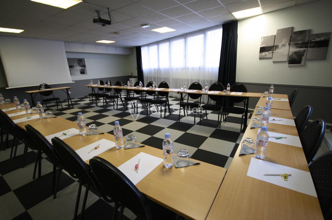 Salle de réunion avec des tables disposées en U, équipées de bouteilles d'eau, stylos et blocs-notes.