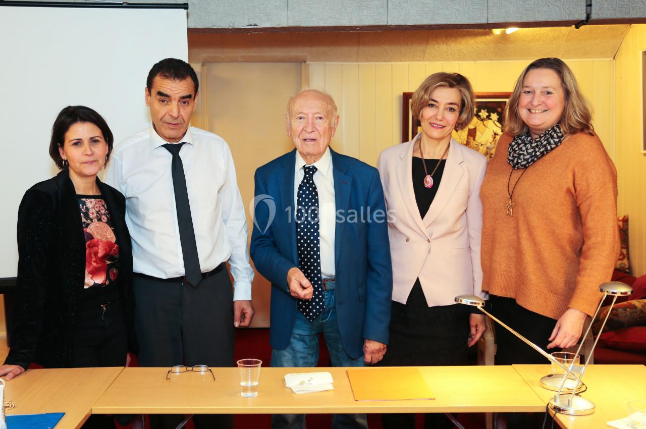 Cinq personnes debout derrière une table dans une salle, posant pour une photo de groupe.