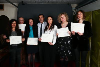 Un groupe de personnes pose devant une bannière, une femme au centre tient un diplôme.