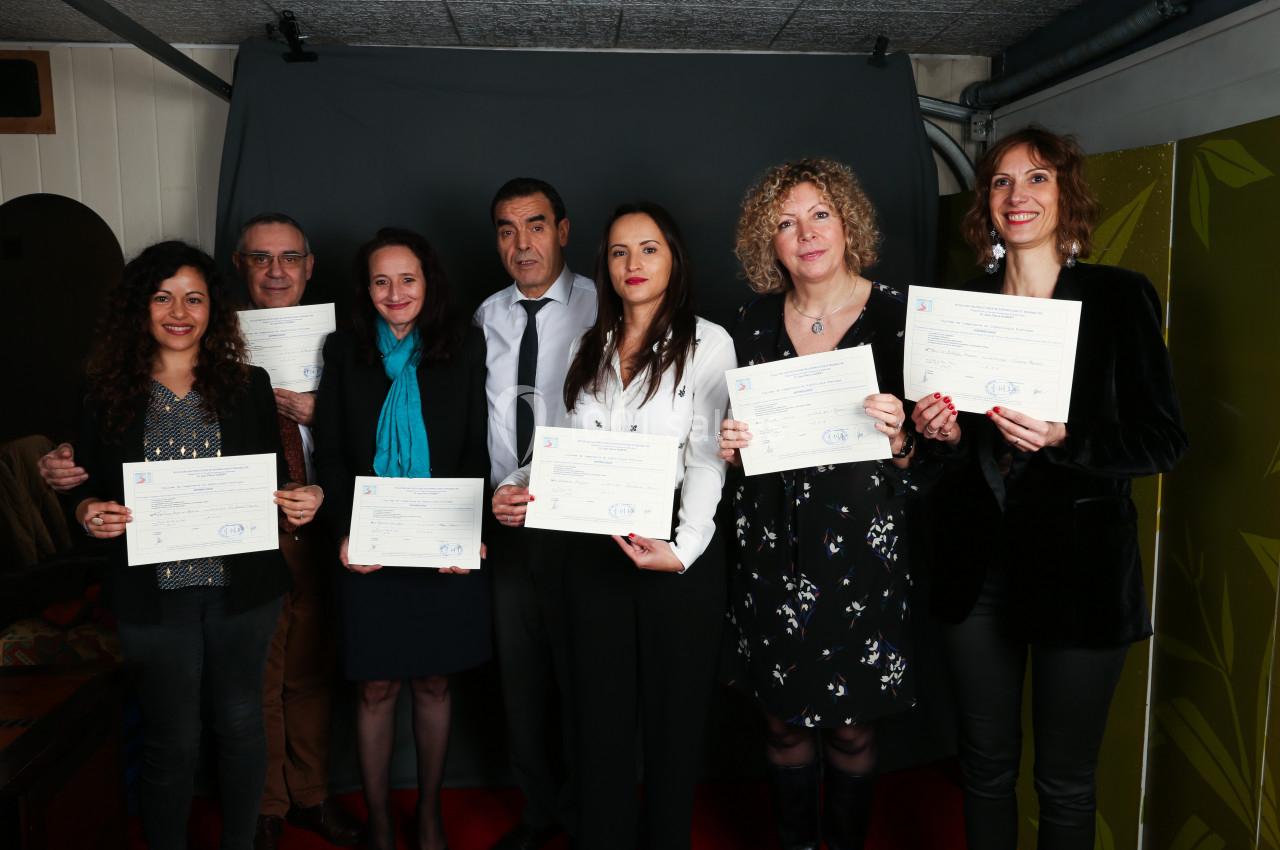 Un groupe de sept personnes pose avec des certificats dans un cadre intérieur devant un fond sombre.