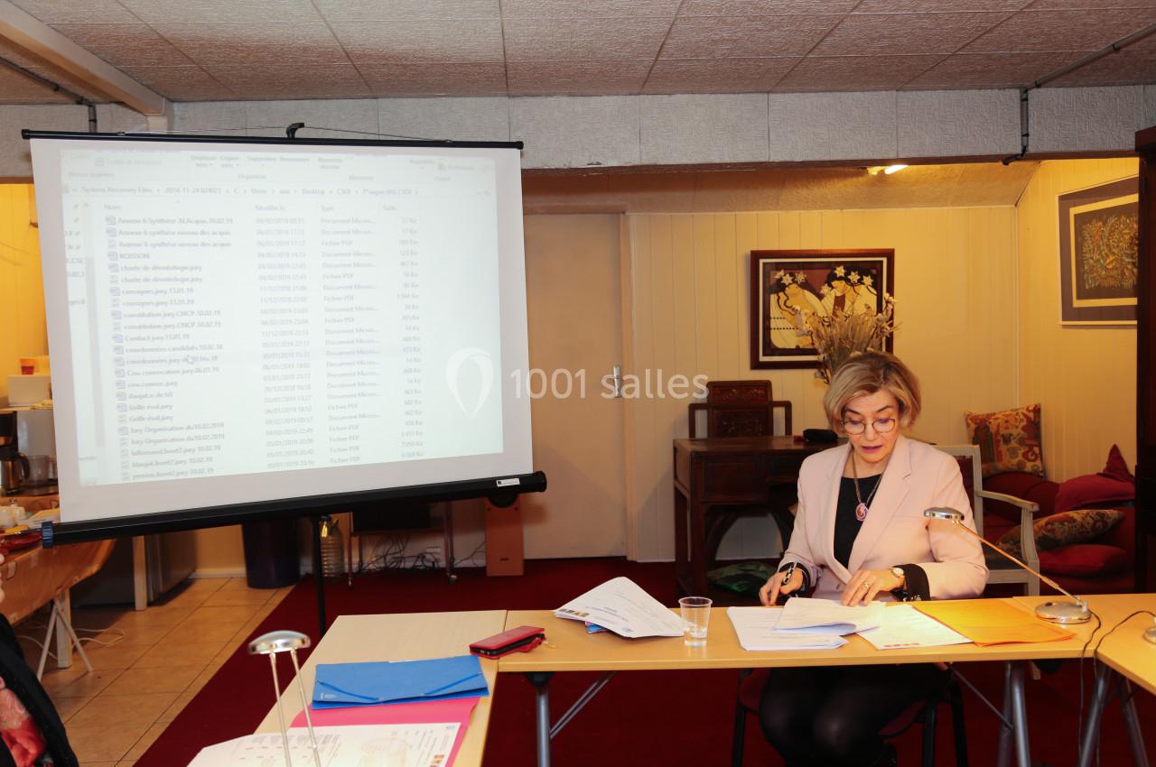 Femme assise à un bureau, prenant des notes, avec un écran de projection affichant un document en arrière-plan.