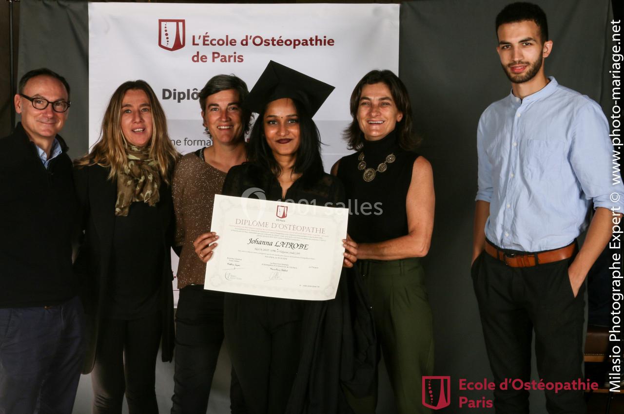 Un groupe de six personnes pose avec une diplômée tenant son certificat devant une bannière d'école d'ostéopathie.