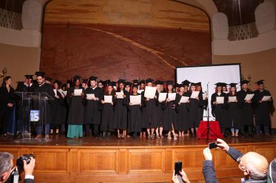 Un groupe de personnes pose devant une bannière, une femme au centre tient un diplôme.
