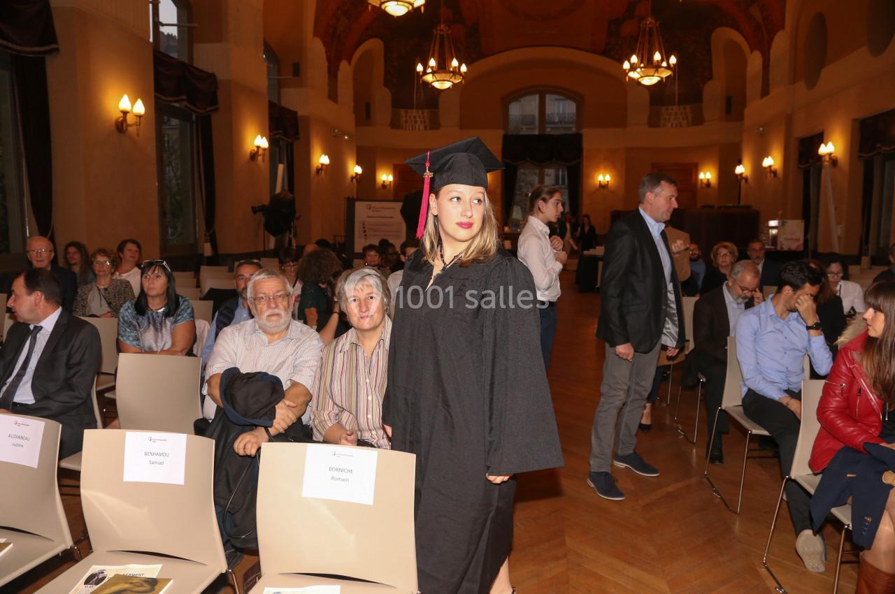 Une femme en toge et toque de diplômée se tient debout dans une salle remplie de personnes assises.