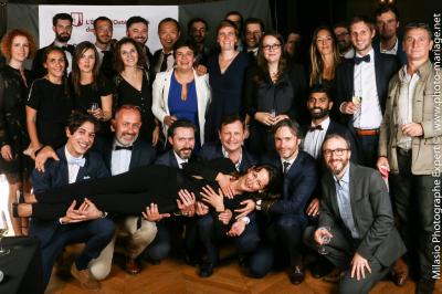 Un groupe de personnes pose devant une bannière, une femme au centre tient un diplôme.