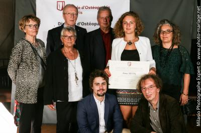 Un groupe de personnes pose devant une bannière, une femme au centre tient un diplôme.