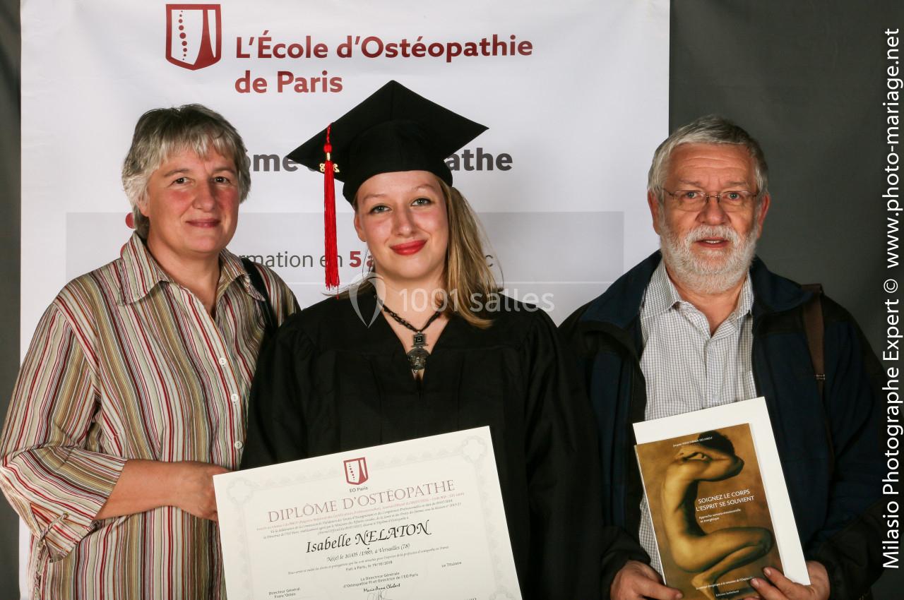 Une diplômée en tenue de cérémonie pose avec deux personnes devant une bannière de l'École d'Ostéopathie de Paris.