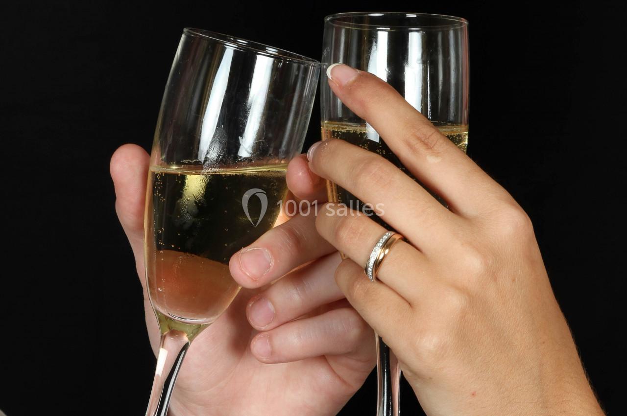 Deux mains trinquent avec des flûtes de champagne, l'une portant une alliance.