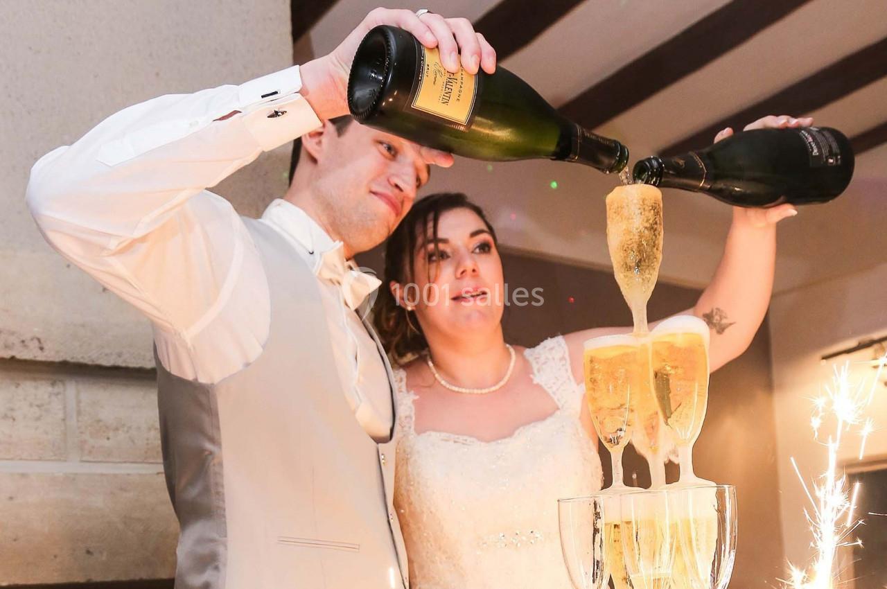 Un couple en tenue de mariage verse du champagne dans une fontaine de verres empilés.