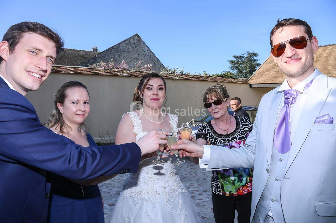 Un groupe de personnes, dont une mariée, trinque dans une cour extérieure par une journée ensoleillée.