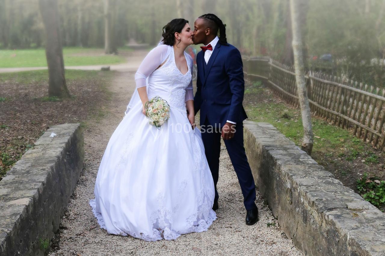 Un couple en tenue de mariage s'embrasse sur un petit pont dans un parc.