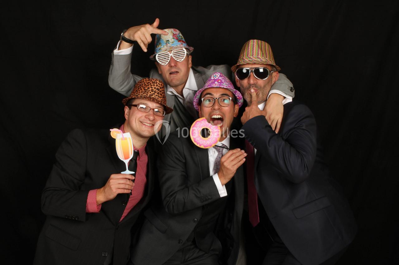 Quatre hommes en costumes posant de manière ludique avec des accessoires festifs sur un fond noir.