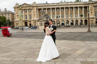 Un couple en tenue de mariage danse sur une place pavée devant un bâtiment historique.