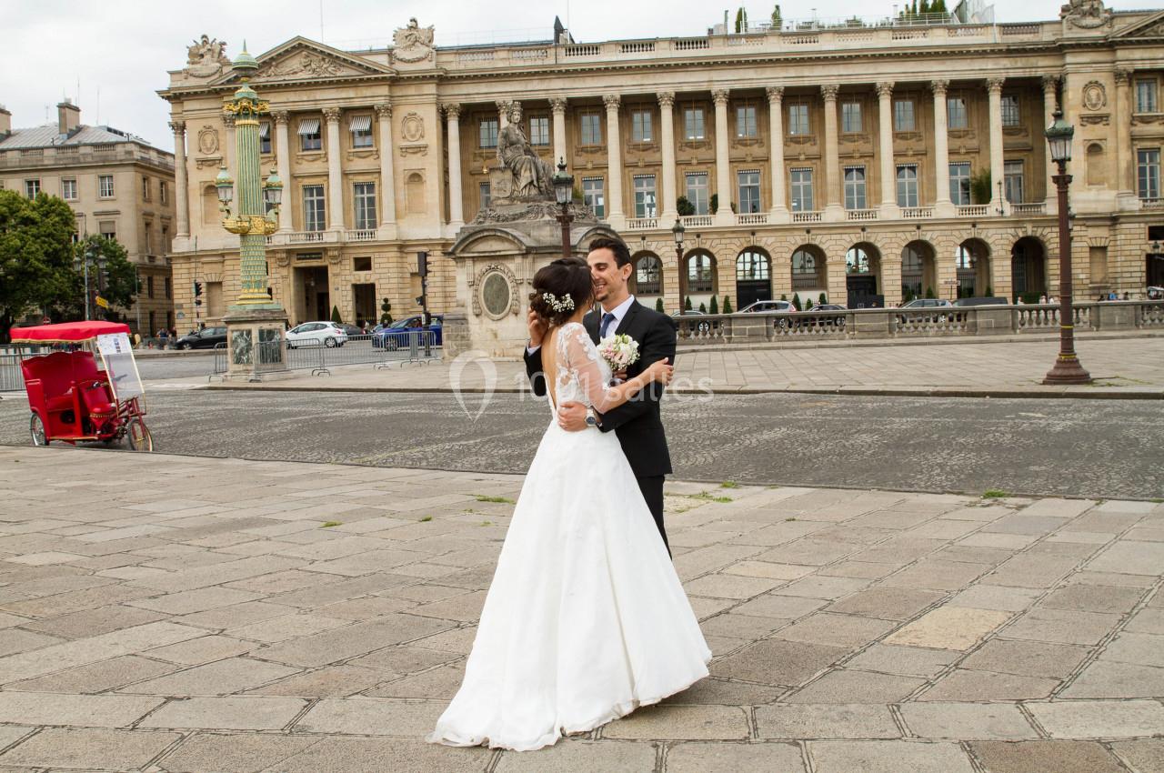 Un couple en tenue de mariage danse sur une place pavée devant un bâtiment historique.
